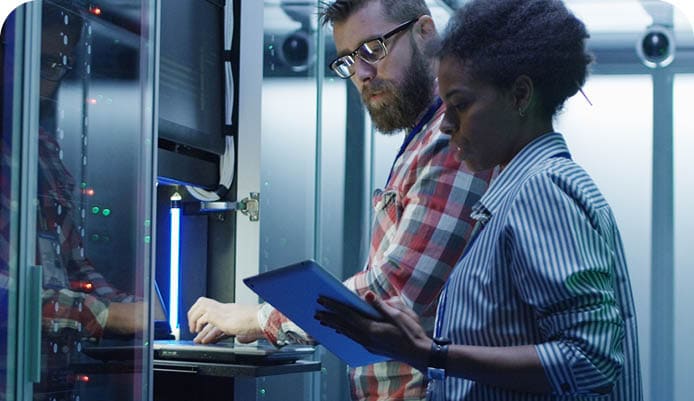 Modern multiethnic man and woman with tablet using laptop in server room while checking servers